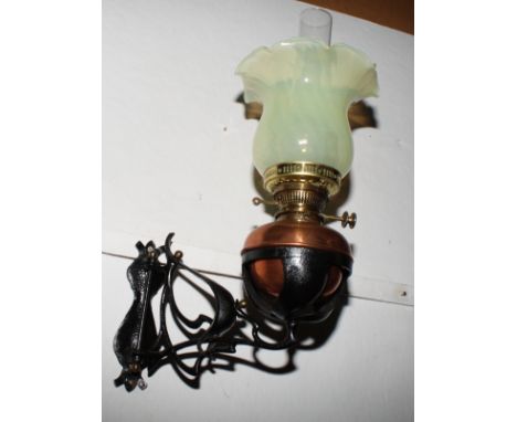 An Art Nouveau wrought iron and copper wall mounted oil lamp with Vaseline glass shade