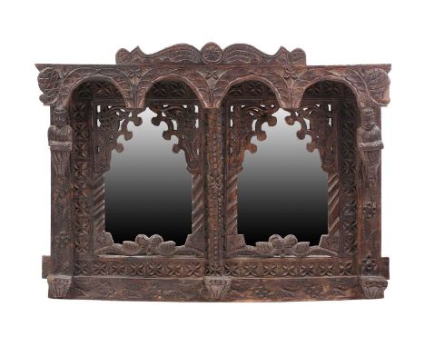 An Indian rustic carved teakwood over mantle mirror with overhanging arcaded cornice above a pair of arched mirror panels fla