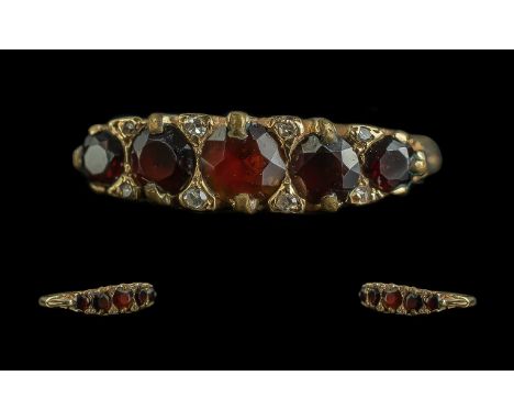 18ct Gold Garnet Ring, set with five graduating round cut garnets between diamond spacers, stamped 18ct.