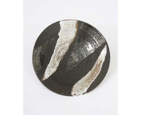 ‡ Janet Leach (1918-1997) a Leach Pottery stoneware plate, resist decorated with simple broad bands, in white on matt black, 