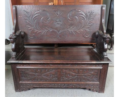 An early 20th century oak monks bench, the hinged top carved to both sides and with winged beast supports and foliate carving