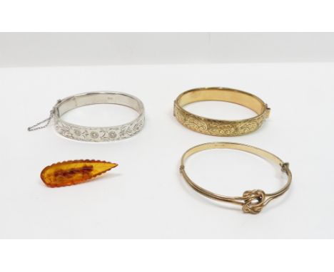 A silver hinged bangle; with two gilt metal bangles; and an amber brooch carved as a leaf
