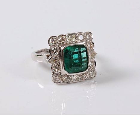 An emerald and diamond cluster ring, the emerald cut emerald, approx. 9.3 x 8.3mm, in a rubover setting, surrounded by round 