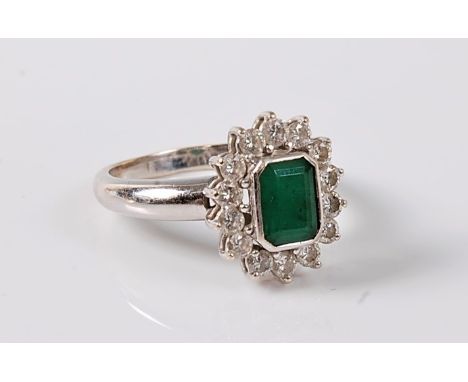 An emerald and diamond cluster ring, the emerald cut emerald in a rubover mount, surrounded by round brilliant cut diamonds, 