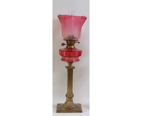 A late Victorian brass pedestal oil lamp, having cranberry tinted acid etched shade and cranberry glass font, to a fluted squ