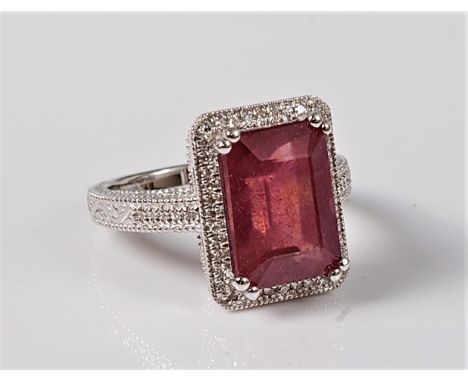 A treated ruby and diamond ring, the emerald cut ruby approx. 11.9 x 8.5mm, in a four claw mount, surrounded by a single row 