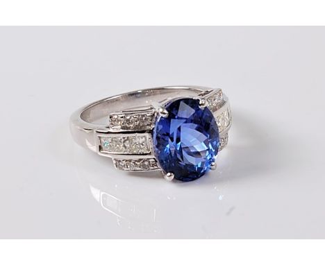 A tanzanite and diamond ring, the oval tanzanite, approx. 11.4 x 9.2 x 6.9mm, set to either side with three stepped channels 