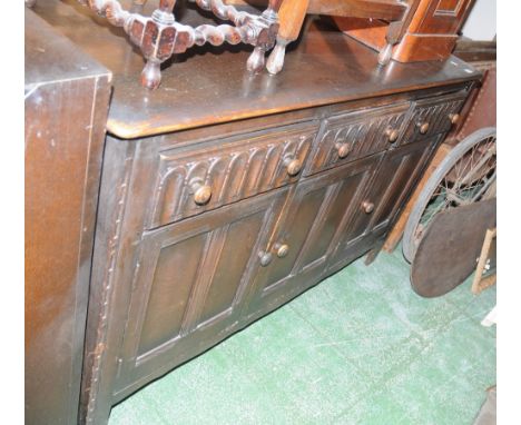 An Ercol dark oak sideboard, three short drawers, fluted fronts over three door cupboard