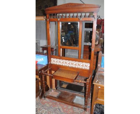 A late Victorian oak hallstand, architectural pediment, spindled back over rectangular plate, tile back above glove box, turn