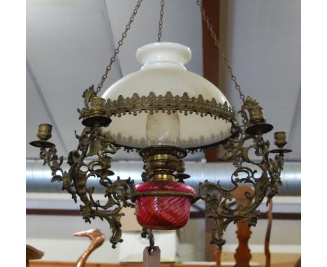 An early 20th century floral pierced and pressed brass hanging oil lamp, having six candle sconces with milk glass shade