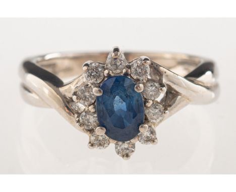 A sapphire and diamond cluster ring, an oval-cut sapphire set to the centre with a surround of brilliant-cut diamonds, marked