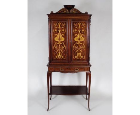 An early 20th century mahogany and marquetry music cabinet on stand, the two marquetry cabinet doors under a low pediment ope