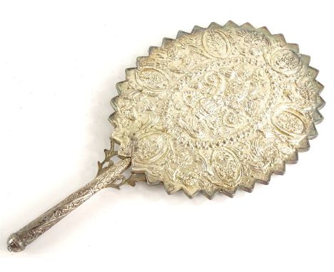 An eastern silver coloured metal hand mirror, embossed with flowers, leaves, etc., and with a jagged edge to the oval frame, 