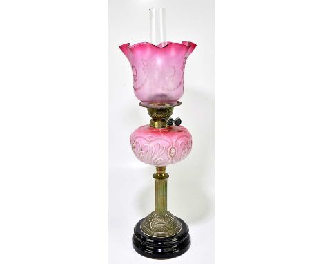A Victorian oil lamp, the cranberry and clear glass shade with etched swags, above the moulded cranberry and milk glass reser