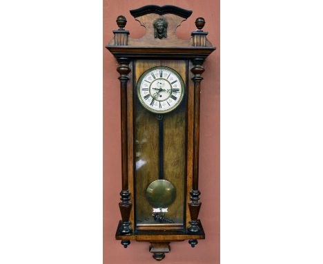 A 19th century rosewood veneered and beech Vienna style wall clock, the shaped pediment with applied mask head and two finial