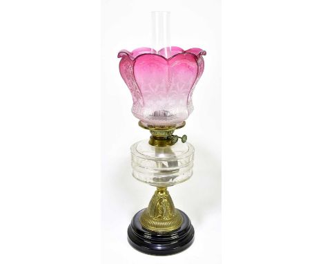 A Victorian oil lamp with cranberry and clear coloured shade, frosted decoration of floral sprays above a faceted glass reser