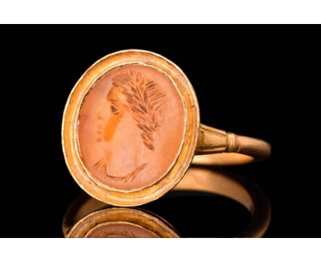 Ca. AD 100 - 300.A gold finger ring of a rounded hoop with decorative shoulders supporting a large bezel set with a stone int