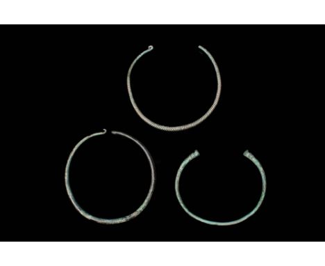 Ca. 200 BC – AD 100.A collection of three Celtic bronze necklaces/torques. The first is a round hoop that widens towards the 