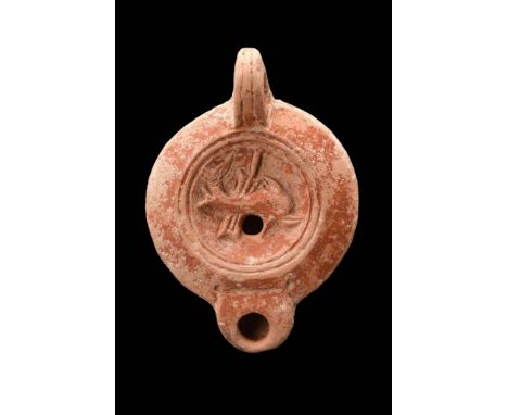 Ca. AD 1 - 100.A terracotta oil lamp boasting a distinctive reddish hue and a charming, recessed tondo adorned with a dolphin