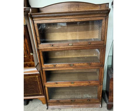 An oak sectional bookcase with an arched three quarter gallery and dentil moulded cornice above four glazed doors with brass 