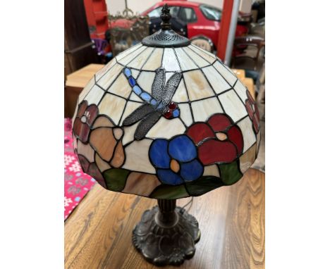 A Tiffany style lamp with a glass shade applied with a dragonfly and flowers on a naturalistic base 