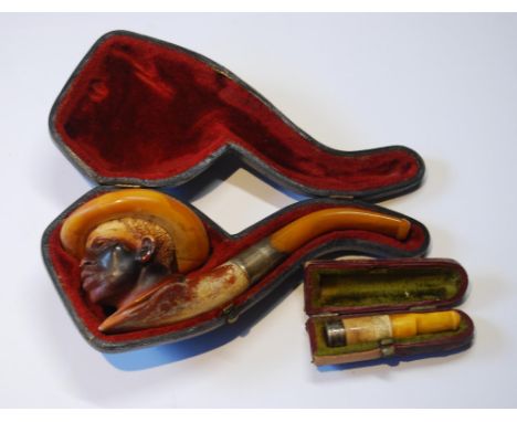 Meerschaum pipe carved as the head of a man with hat, also an amber cigarette holder with silver band, both c. 1900, cased. 