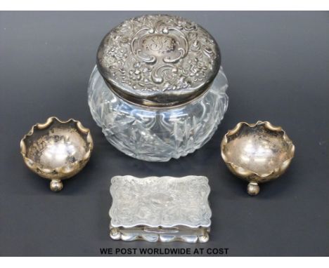 A cut glass pot with a hallmarked silver top, two hallmarked silver open salts and a white metal snuff box with chased decora