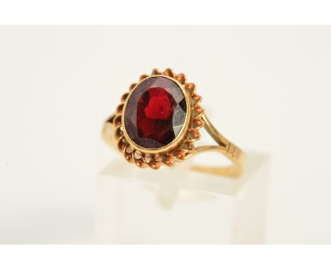 A 9CT GOLD GARNET RING, designed as an oval garnet within a rope twist surround to the bifurcated shoulders, with 9ct hallmar