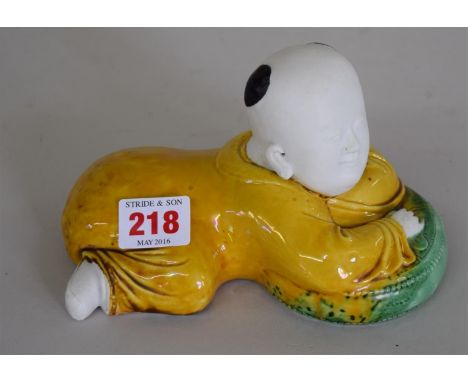A Chinese biscuit and sancai glazed boy, laying on a cushion, 17.5cm wide. Condition Report: In good condition.
