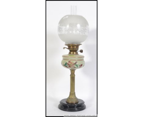 An early 20th century brass and ceramic oil lamp rasied on a two tier circular base with a brass column holding the hand pain