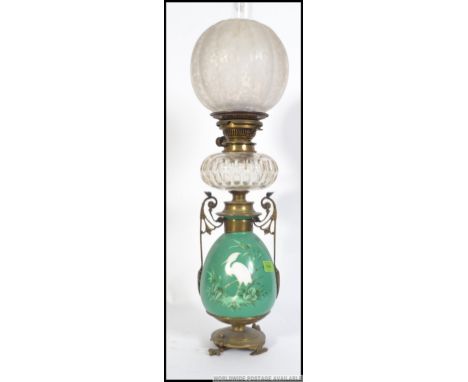 An early 20th century brass and ceramic oil lamp raised on a claw feet base and scroll work handles having a painted ceramic 