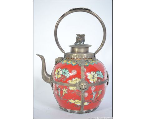 A Chinese ceramic and white metal embellished teapot. The ceramic pot with fu dog masks to the banding, arched handle with fu