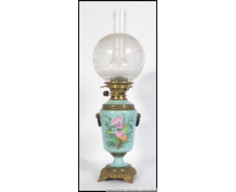 An early 20th century oil lamp rasied on a circular base with feet with a painted ceramic body and reservoir. Complete with e