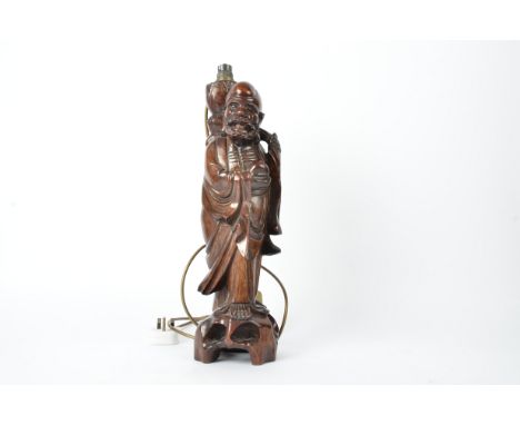 A hardwood Chinese lamp,   in the form of an Immortal holding a  staff and peach, height excluding fixtures 41cm, sold for de
