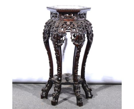 A Chinese carved hardwood stand, hexagonal top with moulded inset, carved and pierced apron, scrolled legs, joined by a shelf