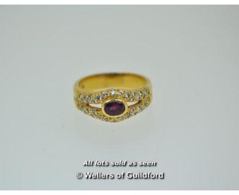 Ruby and diamond cluster ring, oval cut ruby rubover set to the centre with round brilliant cut diamonds set to split shoulde