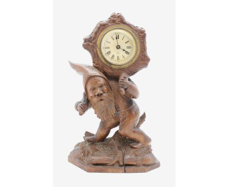 An early 20th Century Black Forest carved wooden mantle clock in the form of a gnome, supporting a circular silvered dial. 23