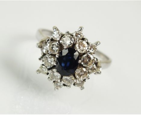 An 18ct white gold sapphire and diamond cluster ring, designed as a central oval mixed cut sapphire claw set within a border 