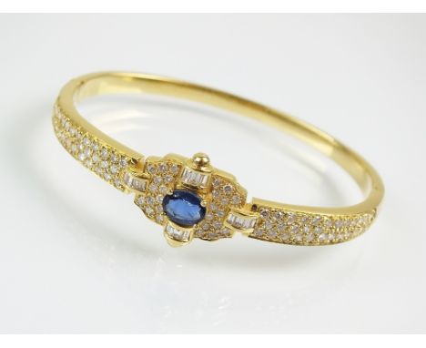 A sapphire and diamond hinged bangle, designed as a central oval mixed cut sapphire flanked by four arches of baguette cut di