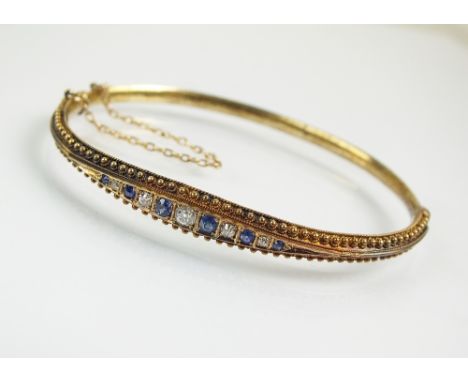 A late 19th century sapphire and diamond hinged bangle, designed as a row of eleven graduated old cut diamonds and sapphires,