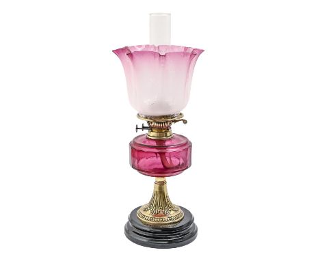 A Victorian stamped brass oil lamp, with faceted cranberry glass fount and brass burner,&nbsp; on black glazed pottery foot, 