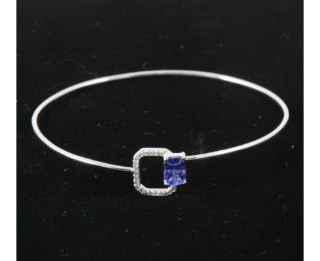 A delicate tanzanite and diamond bangle, the rectangular mixed cut tanzanite 6.8mm x 4.8mm four claw set to one side of a 1.3