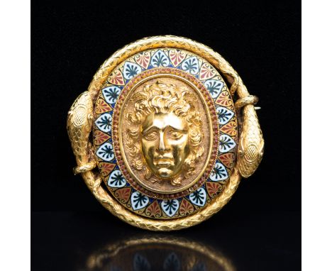 A late 19 th Century yellow metal and enamel oval brooch, with a central mask in high relief within a border of palmettes ena