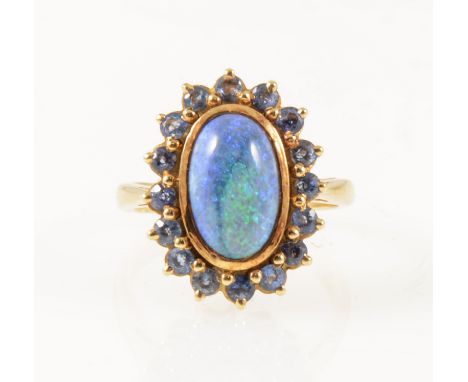 A black opal and sapphire dress ring, the oval cabochon cut opal 13mm x 8mm collet set and surrounded by sixteen claw set bri