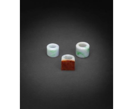 TWO JADEITE AND ONE PALE GREEN AND RUSSET JADE THUMB RINGSQing DynastyOne ring with a flat square face with orange-russet ton