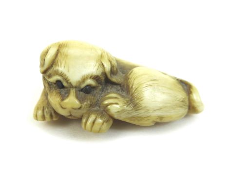 A Japanese ivory netsuke of a puppy, circa 1900, modelled in recumbent pose, unsigned, 5 by 3.5 by 2.2cm high. 