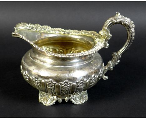 A George IV silver milk jug, with profuse repousse and applied decoration, raised on four shell and foliate form feet, bearin