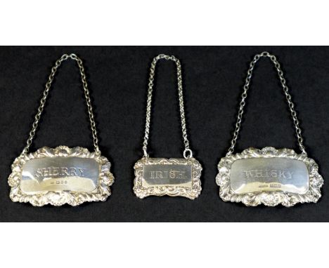 A group of three silver decanter labels, each with cast foliate decorative borders, comprising a small George V silver label 