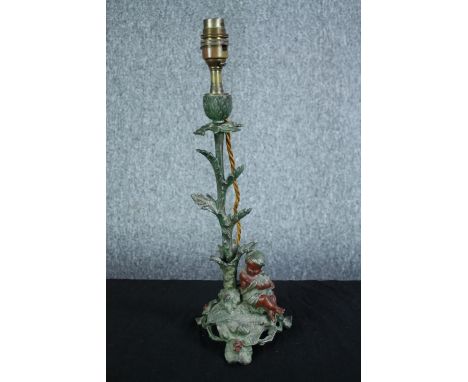 A metal lamp in the shape of a flower stem with a cherub seated at the base. Patinated and painted brass. Stamped 'E.P' at th