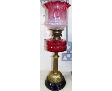 A 19th century brass reeded column oil lamp with cranberry reservoir and shade (shade a.f.)